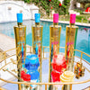Gold bottles with colorful caps on a reflective surface near a pool
