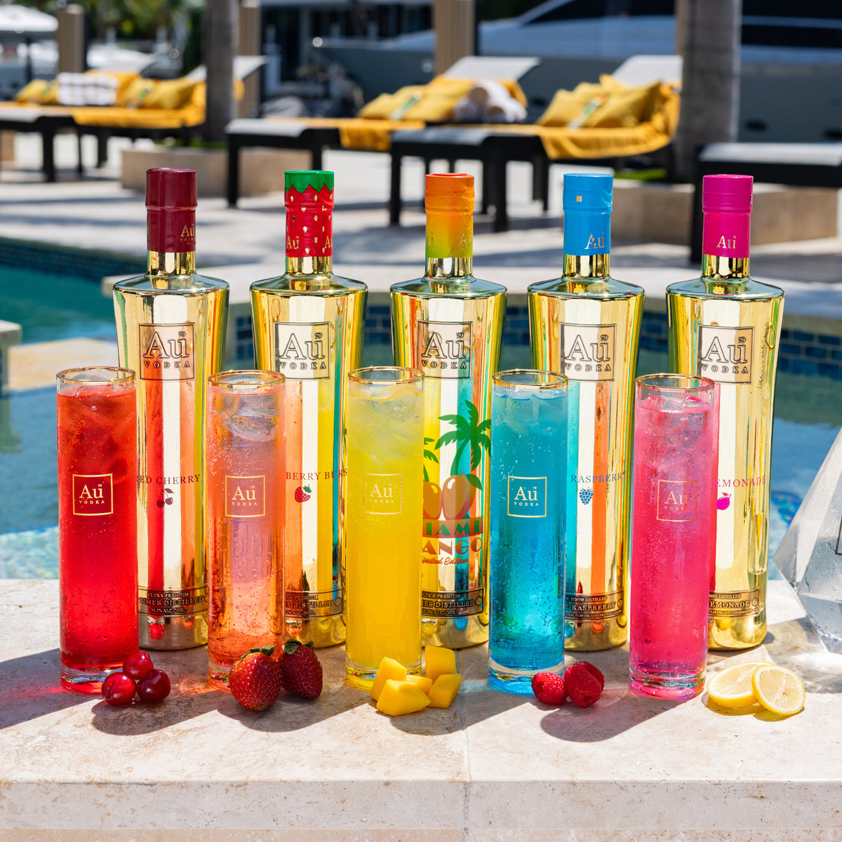Au Vodka bottles and cocktails by a pool with fruit garnishes
