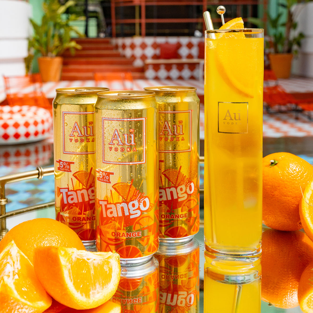 Au Vodka Tango Orange cans and a tall glass of orange drink with orange slices and a gold stirrer