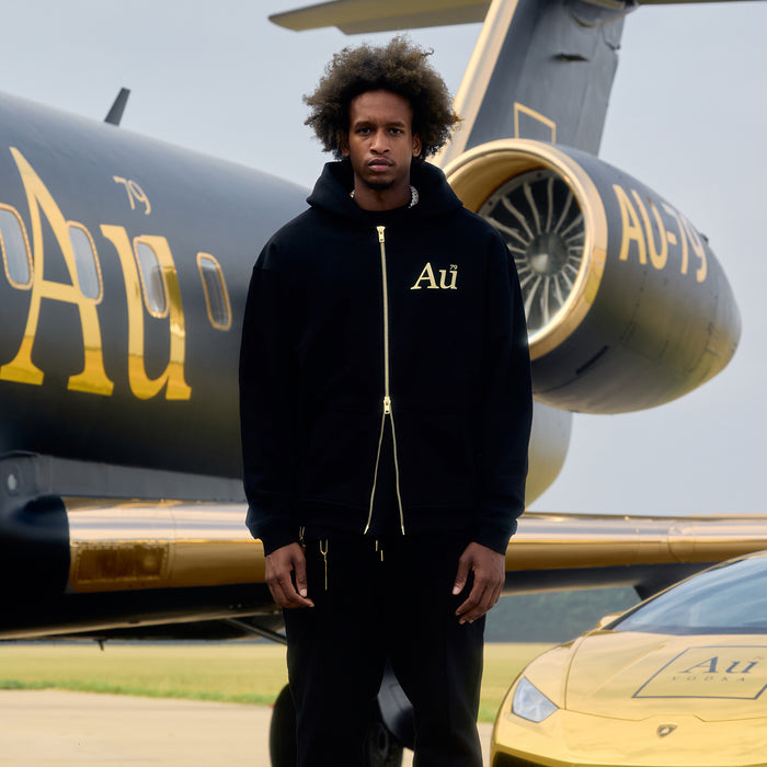 Man standing in front of a luxury car and a jet with 'Au' branding.