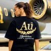 Person wearing a black t-shirt with gold and white text in front of a black and gold airplane.