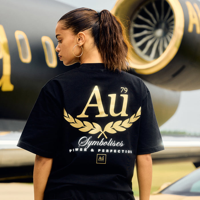 Person wearing a black t-shirt with gold and white text in front of a black and gold airplane.