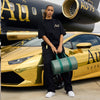 Person holding a green handbag in front of a gold car and black airplane with 'Au' branding.