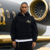 Person wearing a black hoodie with gold 'Au' lettering in front of a luxury airplane.