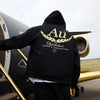 Person wearing a black hoodie with gold 'Au' text in front of a private jet