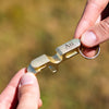 Gold keychain tool held by a hand with a blurred natural background