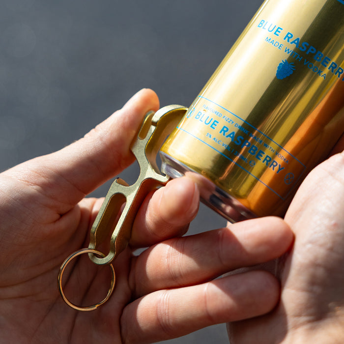 Gold can opener held by a hand with a blue raspberry drink in the background
