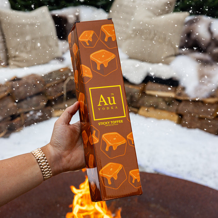 Person holding a box of Au Vodka Sticky Toffee by a fire
