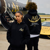 Two people wearing black hoodies with 'Au' logo in front of a jet