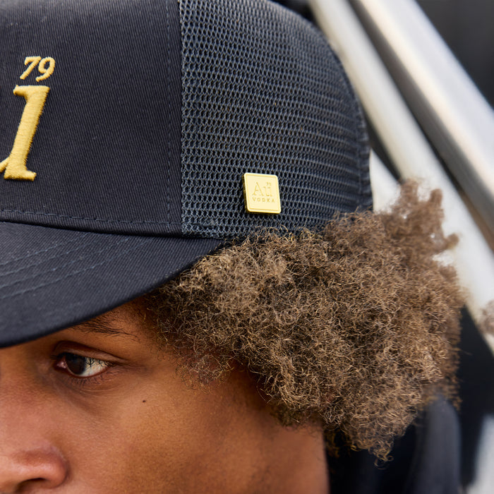 Close-up of person wearing a black hat with gold accents and a logo.