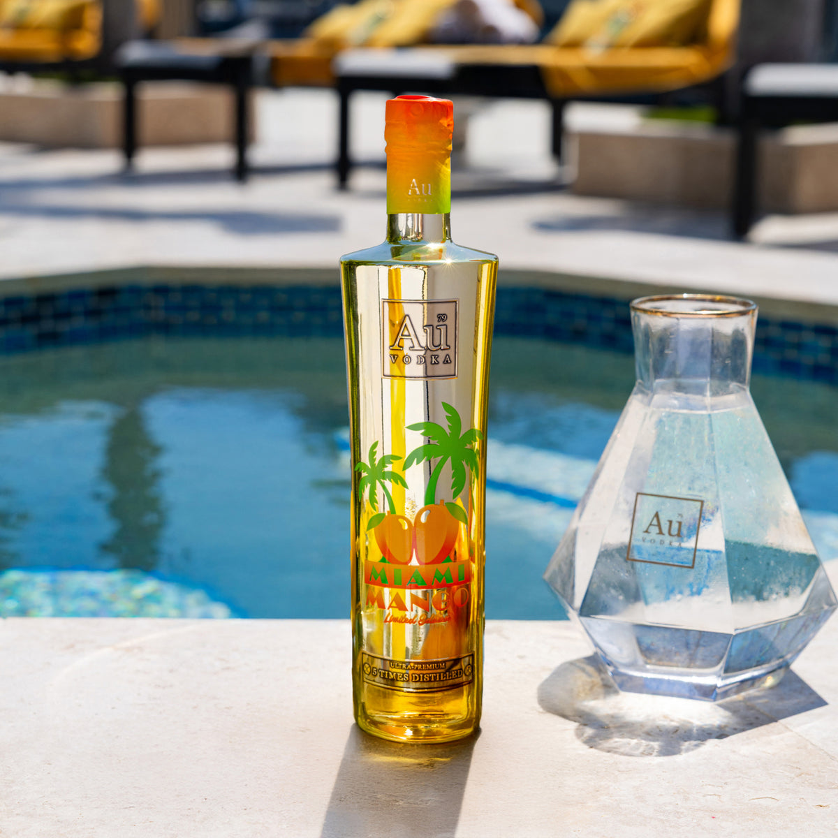 Au Vodka Miami Mango bottle and a clear decanter by a pool