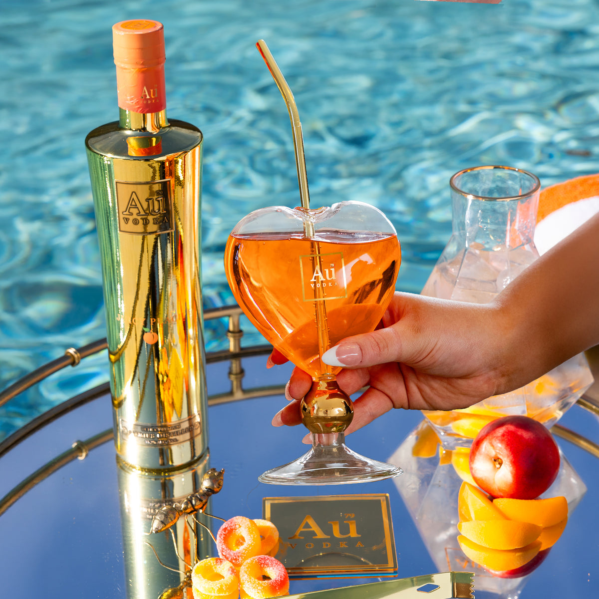 Au Vodka bottle and heart-shaped glass with a drink, on a mirrored tray by a pool