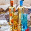 Two bottles of Au Vodka, one gold and one blue, with glasses filled with the respective colors on a snowy background.
