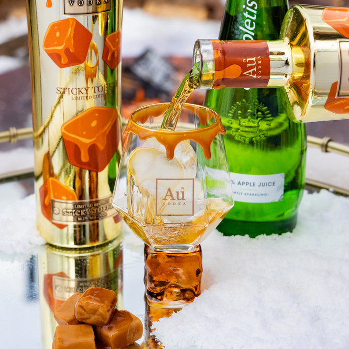 Alcohol being poured into a glass with bottles and candy in the background