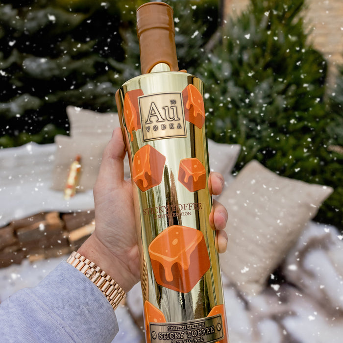 Bottle of Au Vodka with sticky toffee flavor held by a person outdoors.