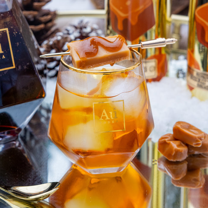 Glass of iced coffee with a caramel square on a skewer, surrounded by bottles and caramel candies.