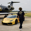 Man walking towards a gold sports car and airplane on a runway with 'AU' branding.